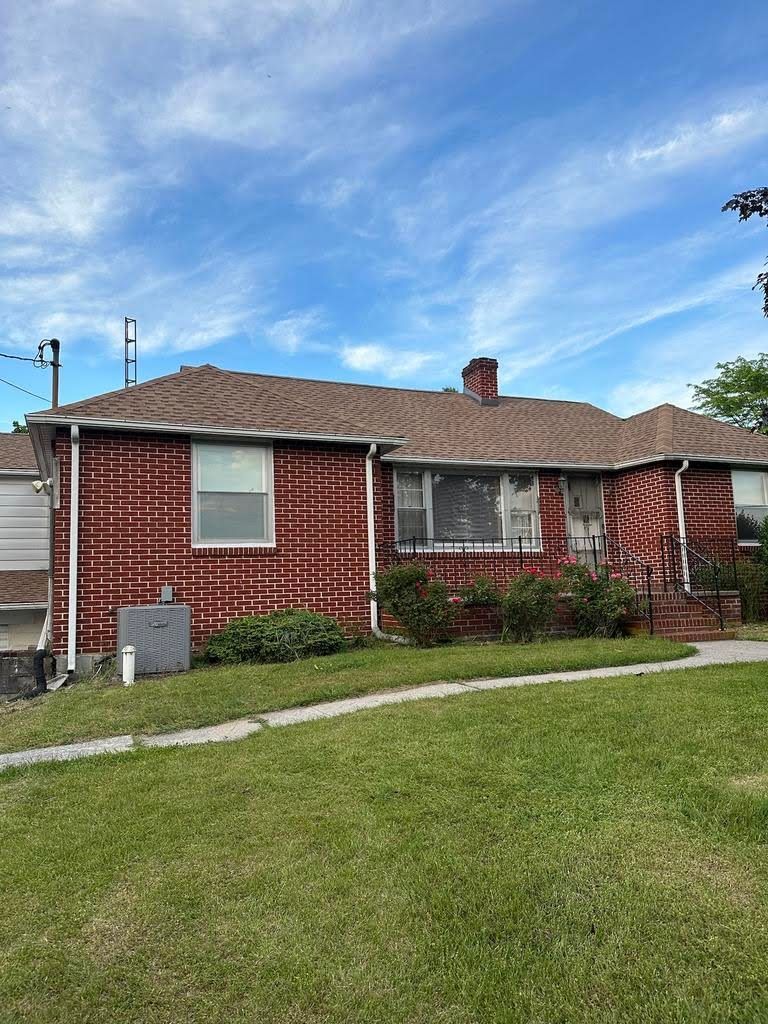 A red brick house with a brown roof is sitting on top of a lush green lawn.