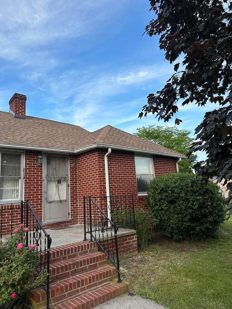 A brick house with stairs leading up to the front door and a tree in front of it.