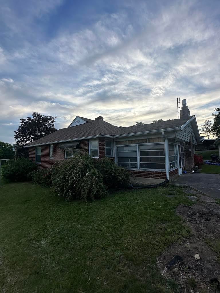 A house with a lot of windows is sitting in the middle of a lush green field.