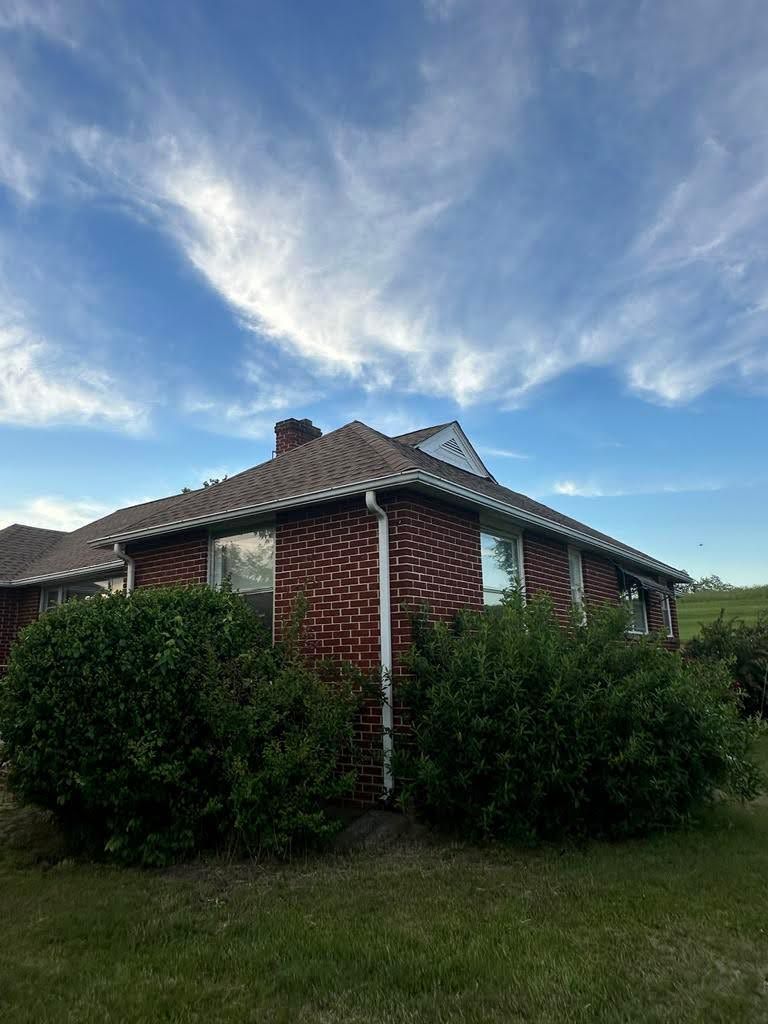 A brick house is surrounded by bushes and shrubs on a sunny day.