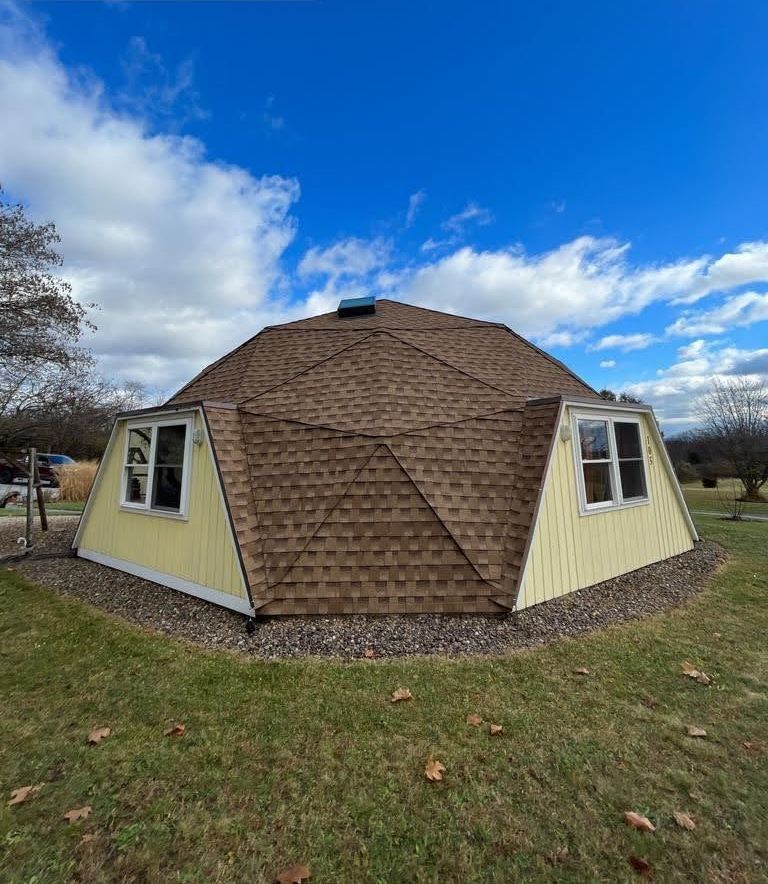 A dome house with a brown roof is sitting in the middle of a grassy field.