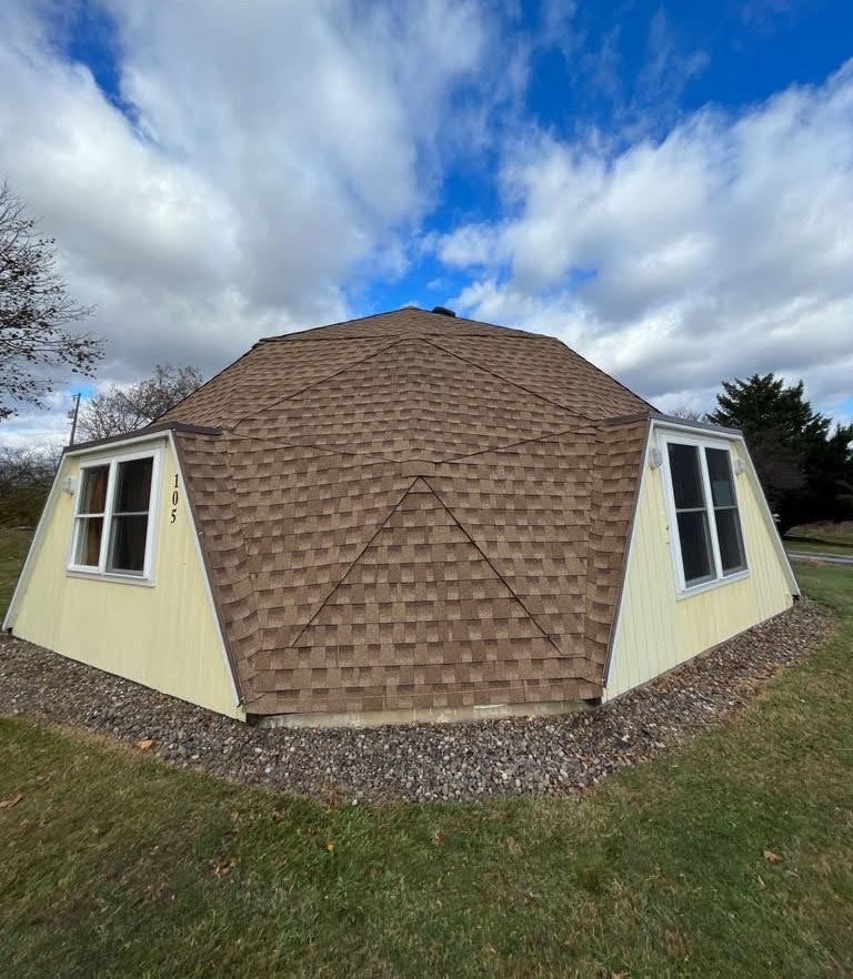 A dome shaped house with a brown roof is sitting in the middle of a grassy field.