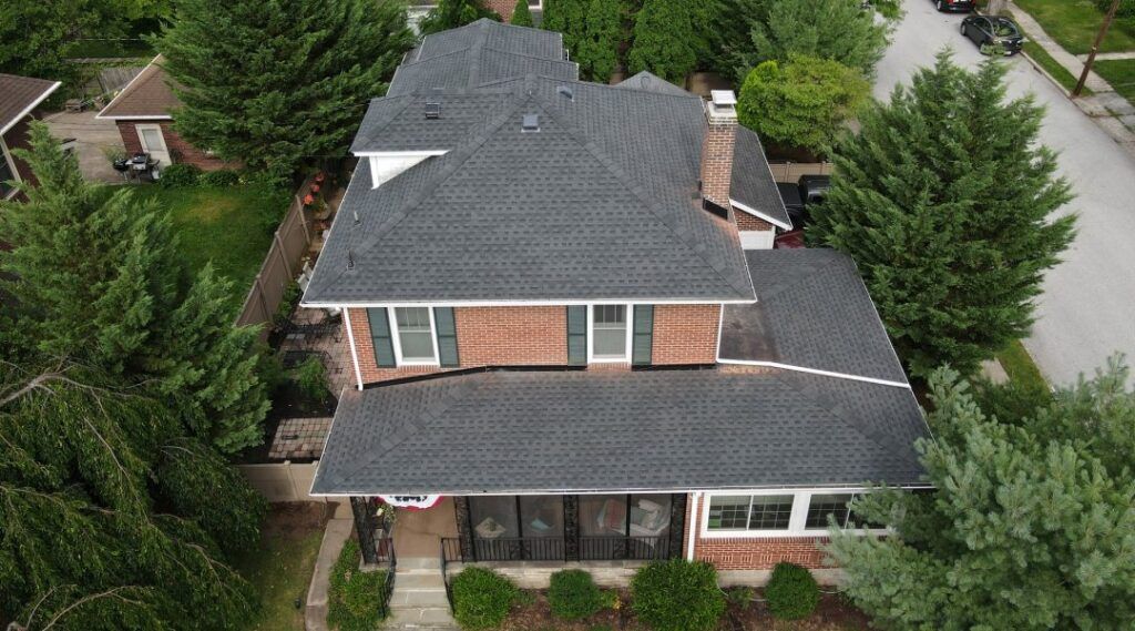 An aerial view of a large brick house with a gray roof surrounded by trees.