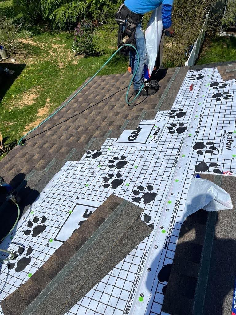 A man is standing on top of a roof with a hose.