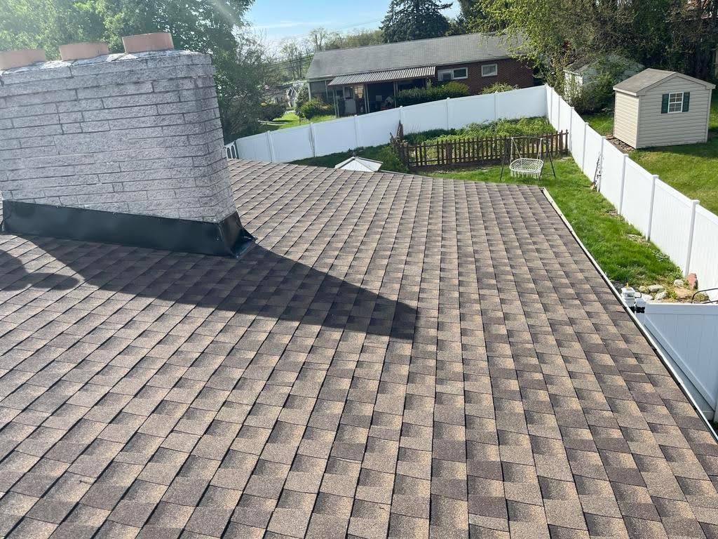 A roof with a chimney and a white fence in the background.