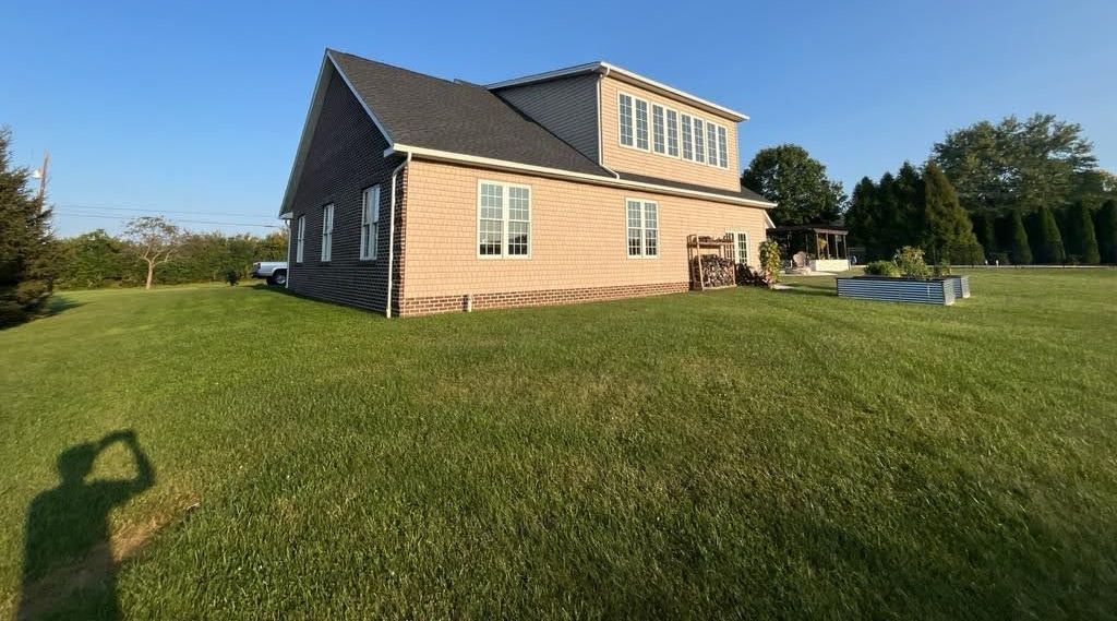 A large brick house is sitting in the middle of a lush green field.