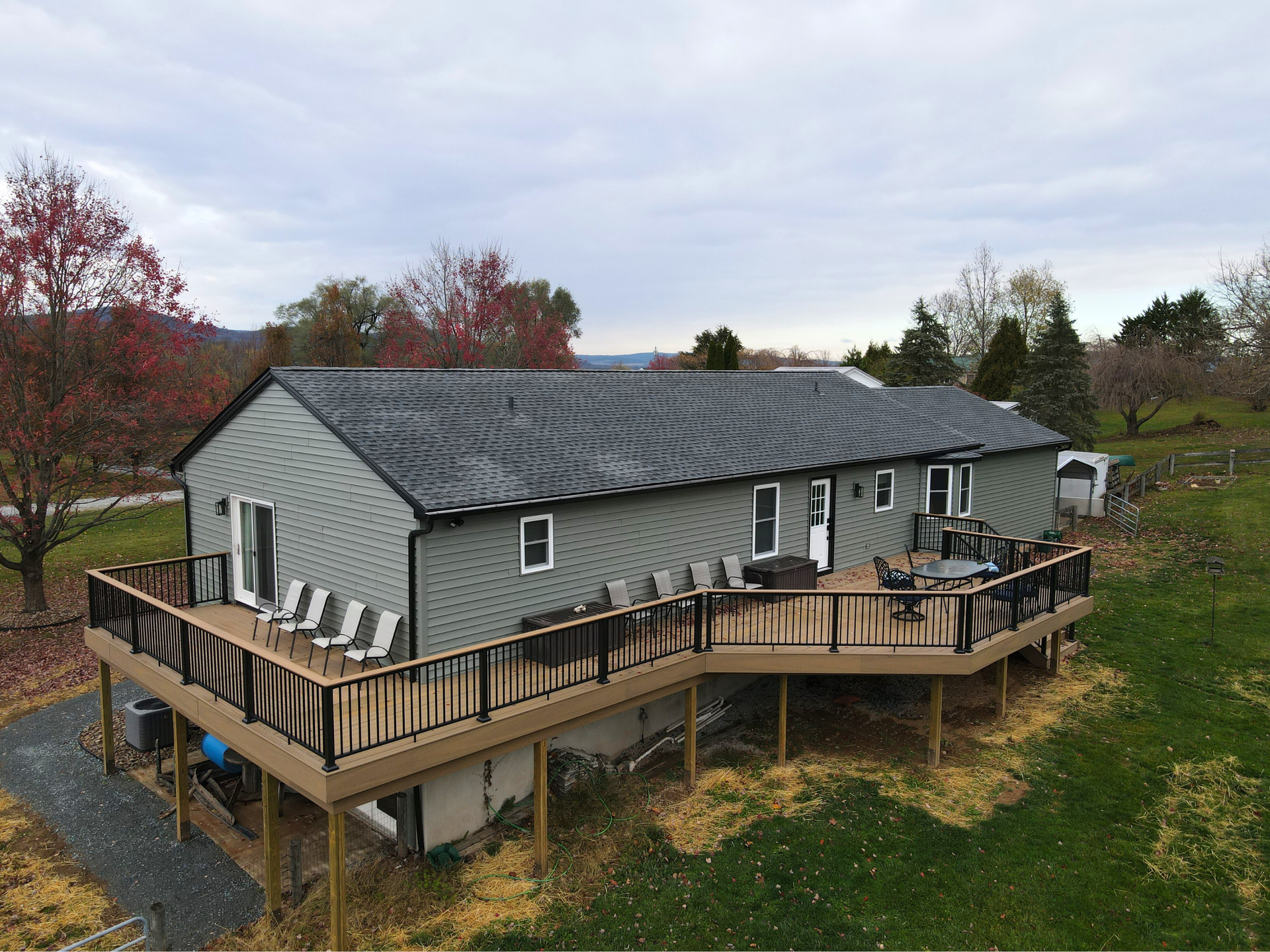 An image of a home with a gray roof, muted green siding, and a custom wrap-around second-story deck by Dayhoff Construction.