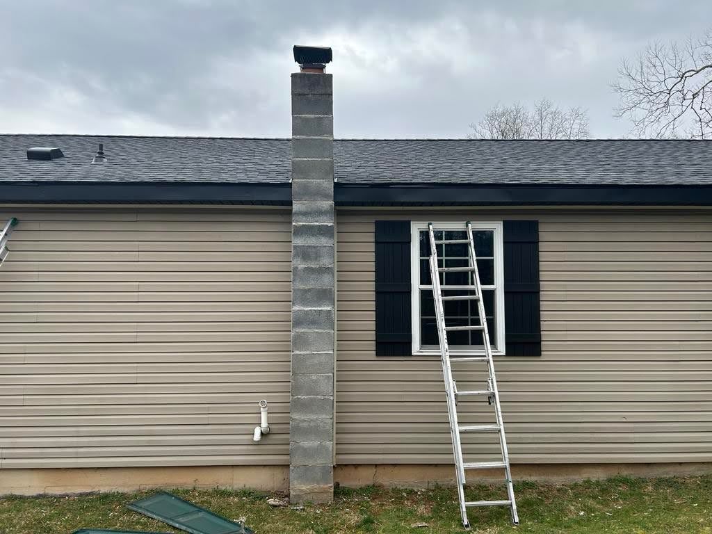 A ladder is sitting on the side of a house next to a chimney.