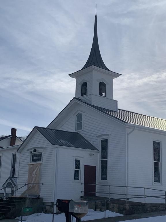 White church building with a tall steeple under a cloudy sky. There's snow on the ground.