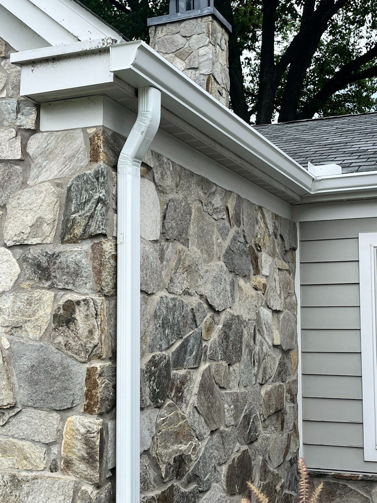 A house with a stone wall and a white gutter on the side.