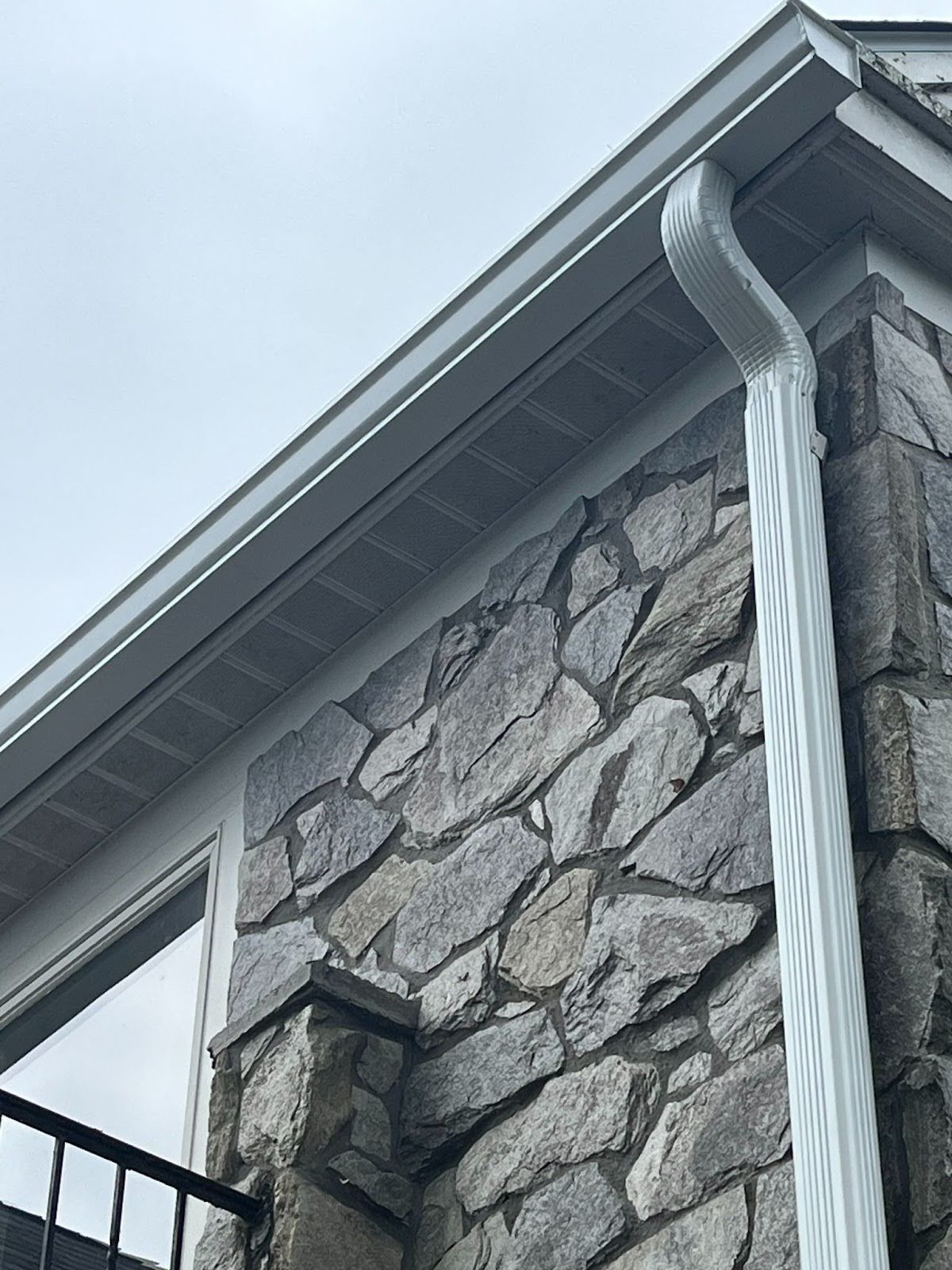 A white gutter is on the side of a stone building.