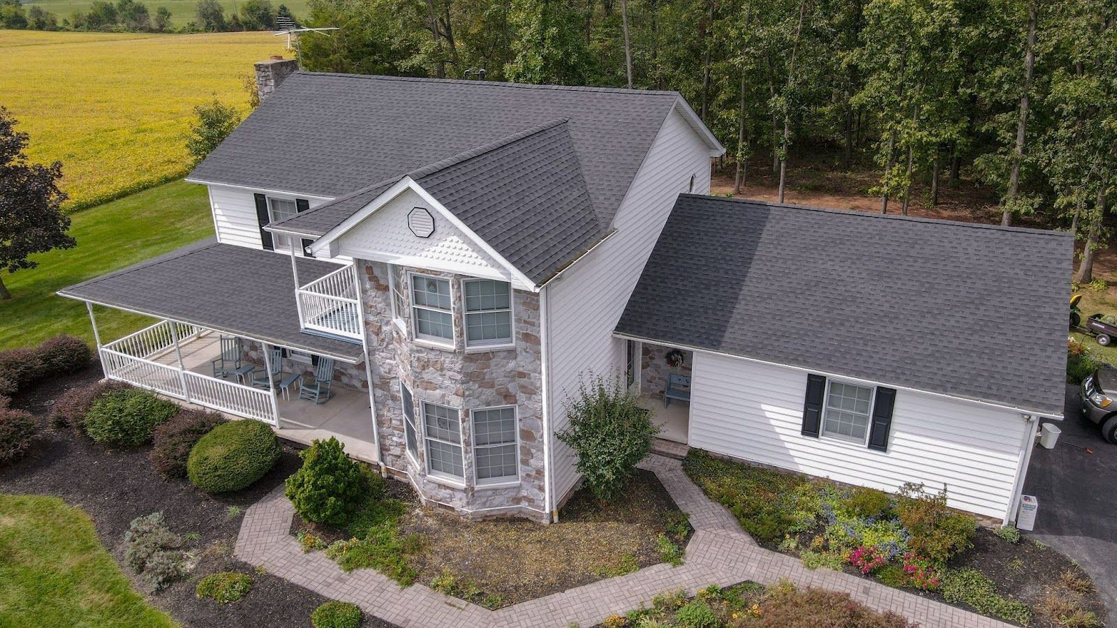 An aerial view of a large white house with a black roof surrounded by trees.