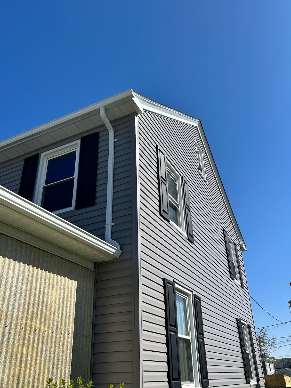 A large gray house with black shutters and a blue sky in the background.