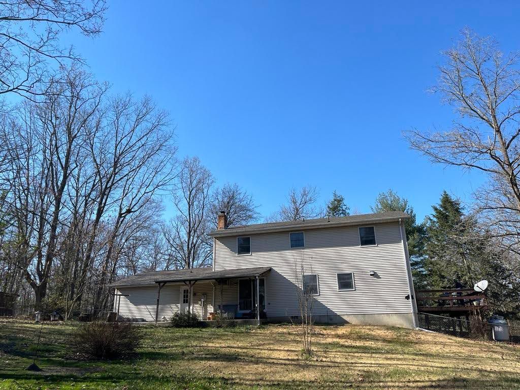 A large white house with a porch is surrounded by trees on a sunny day.