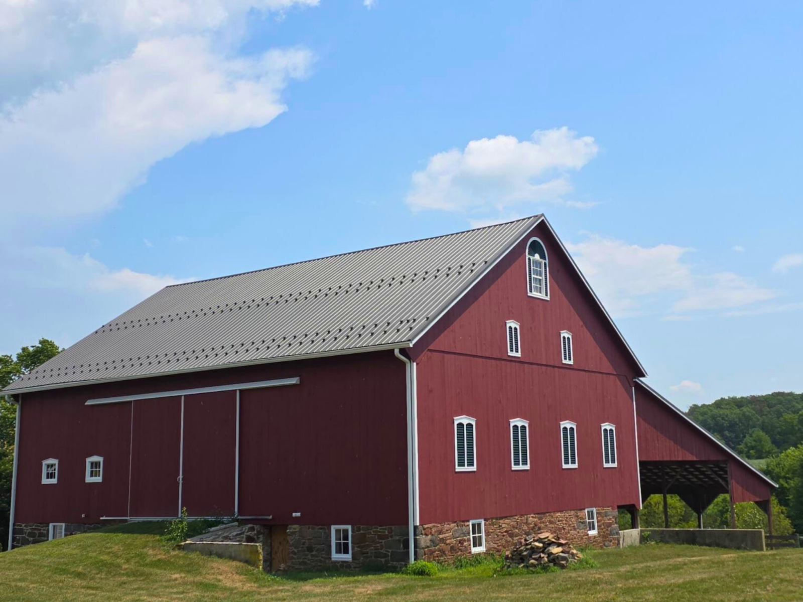 A large red barn with a gray roof is sitting in the middle of a grassy field.
