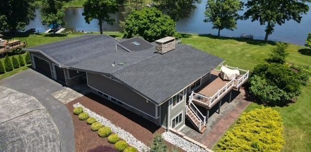 An aerial view of a house with a deck and a lake in the background.