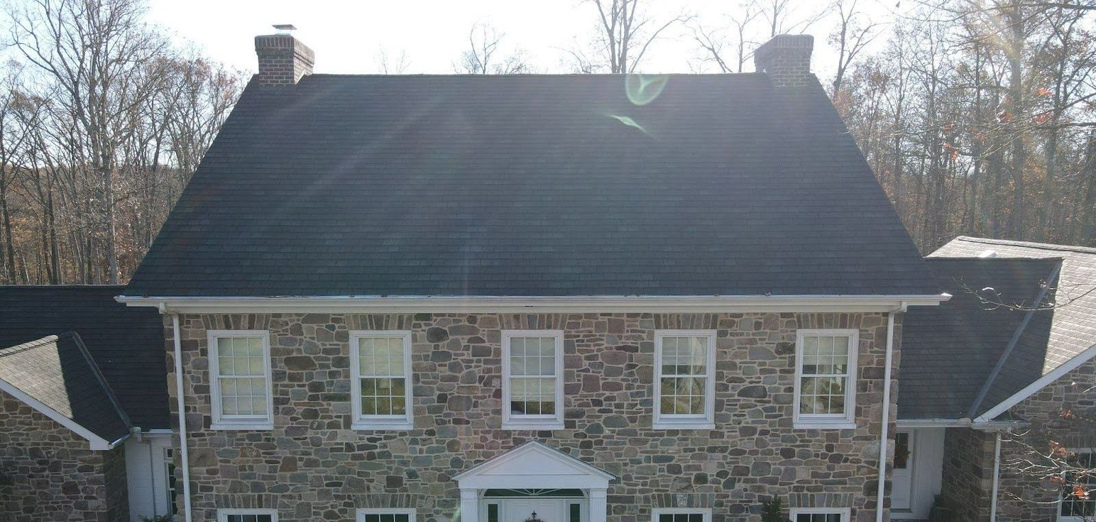 A large stone house with a black roof is surrounded by trees.