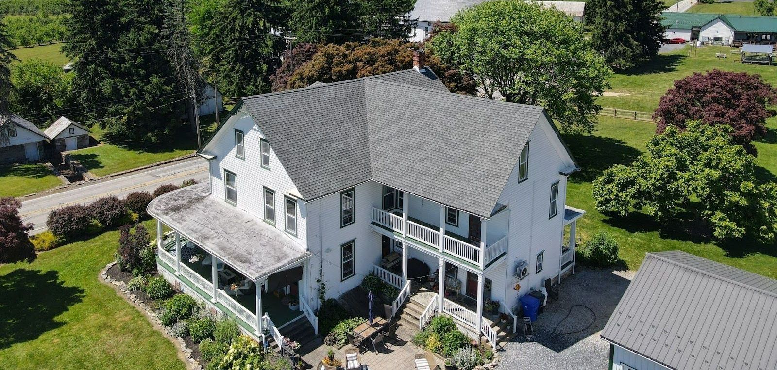 An aerial view of a large white house with a porch surrounded by trees.