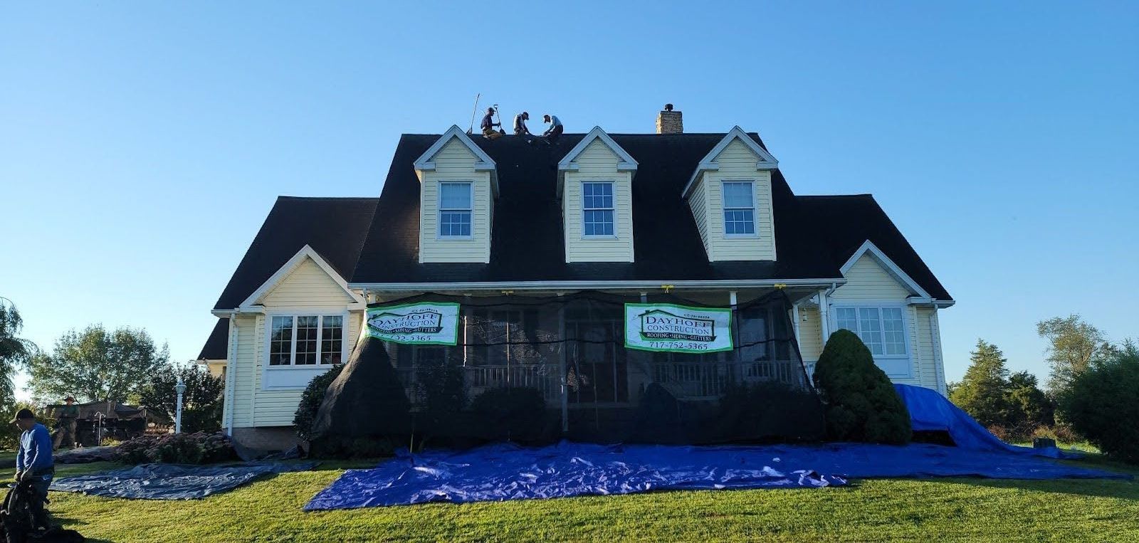 A large white house with a black roof is being remodeled.