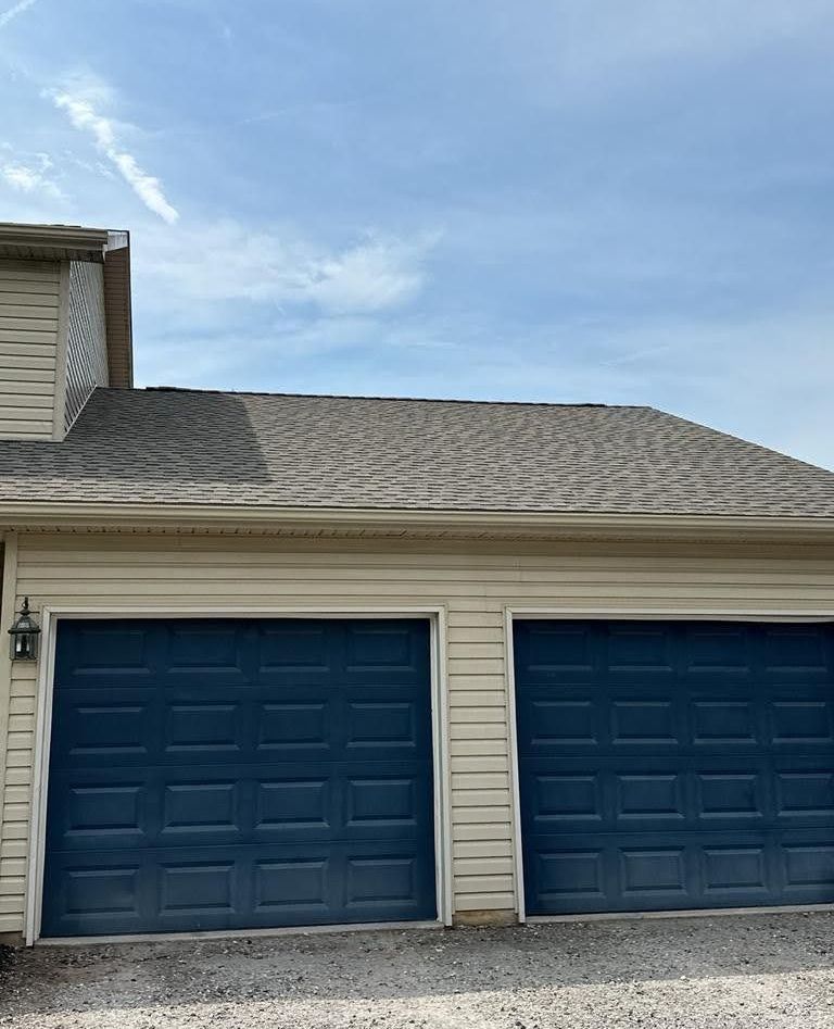 A house with two blue garage doors and a blue sky in the background.