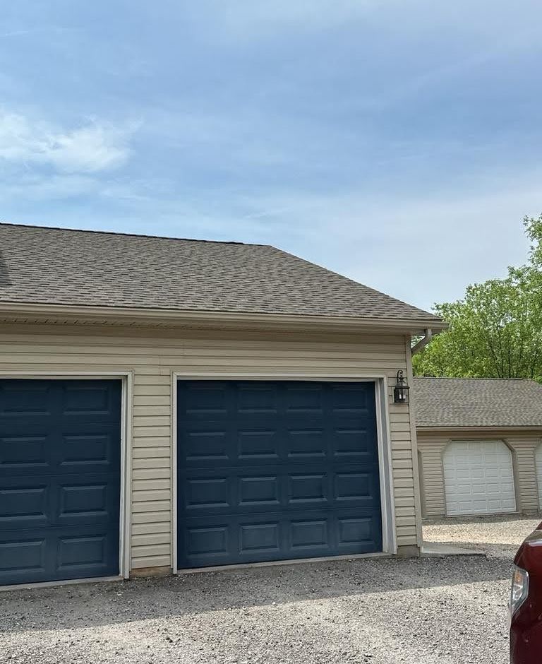 A car is parked in front of a garage with blue garage doors.
