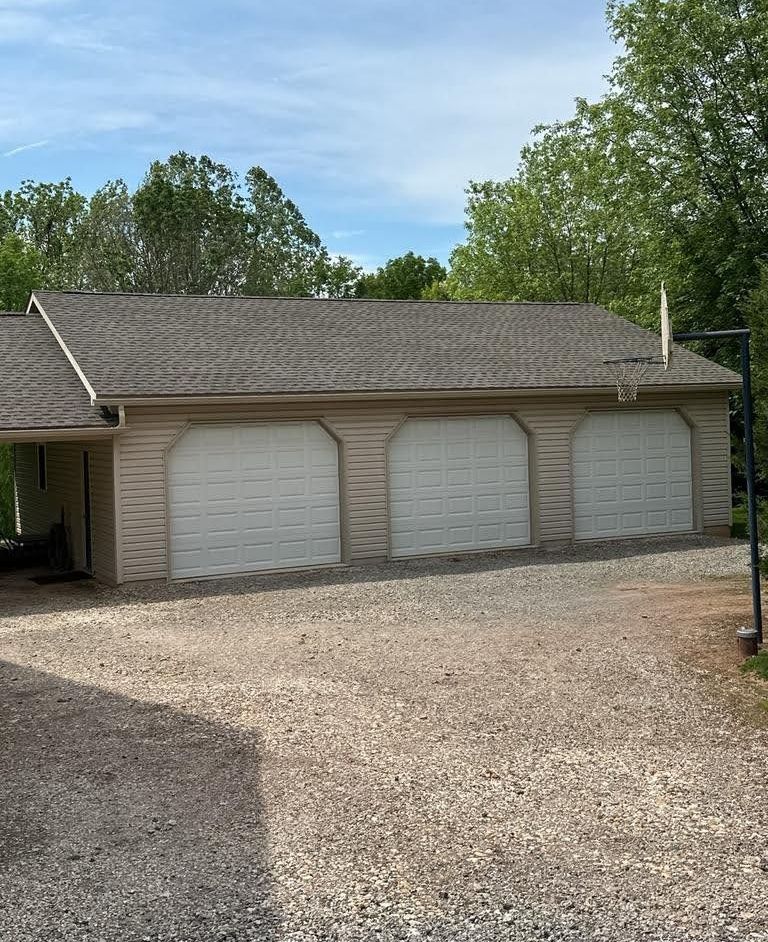 A garage with three white garage doors and a gravel driveway