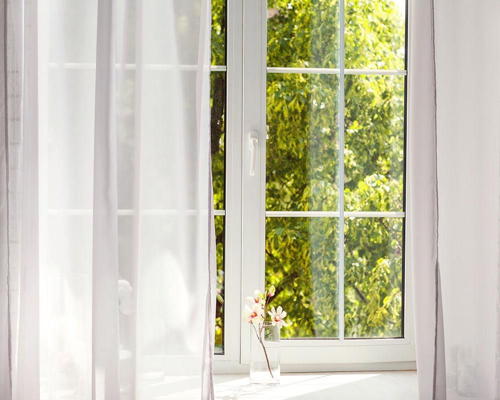 A window with white curtains and a vase of flowers on the window sill.