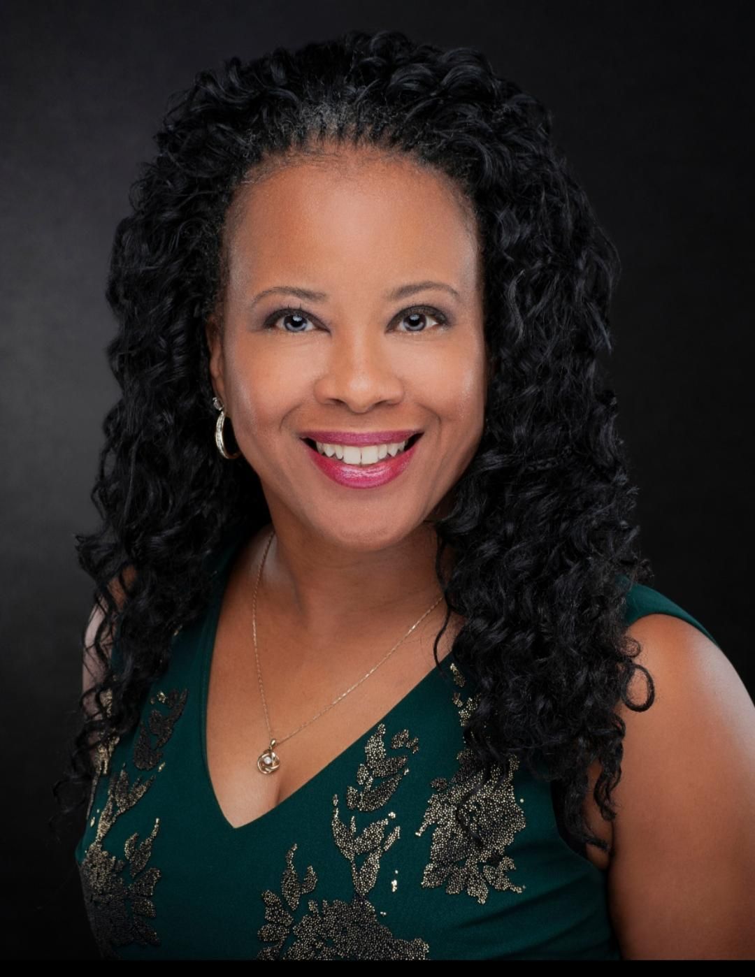 A woman is sitting at a desk with a laptop and a vase of flowers.