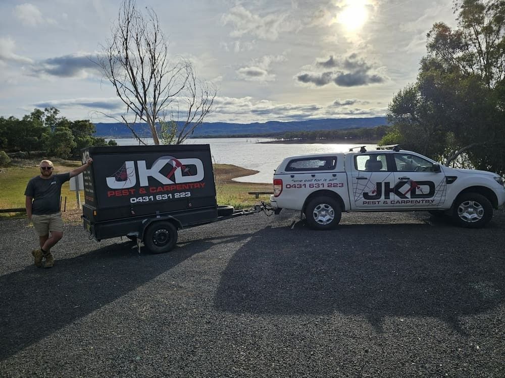 A Man is Standing Next to a Truck With a Trailer Attached to It — JKD Pest & Carpentry In Wellington, NSW