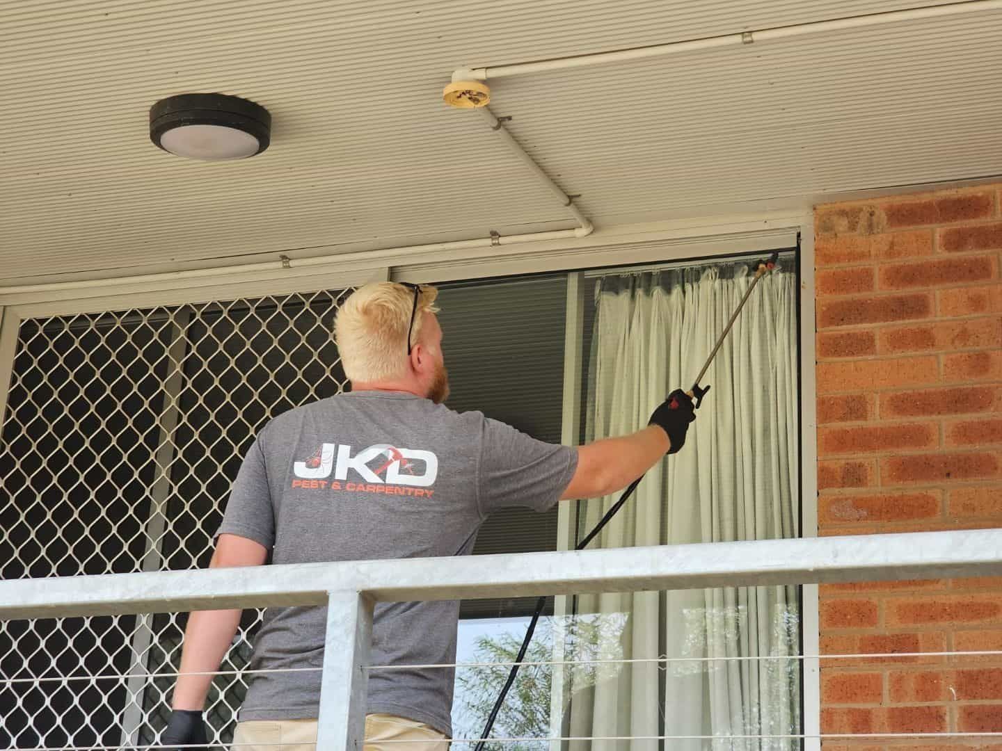 A Man Wearing a Jkd Shirt is Cleaning a Window — JKD Pest & Carpentry In Wellington, NSW