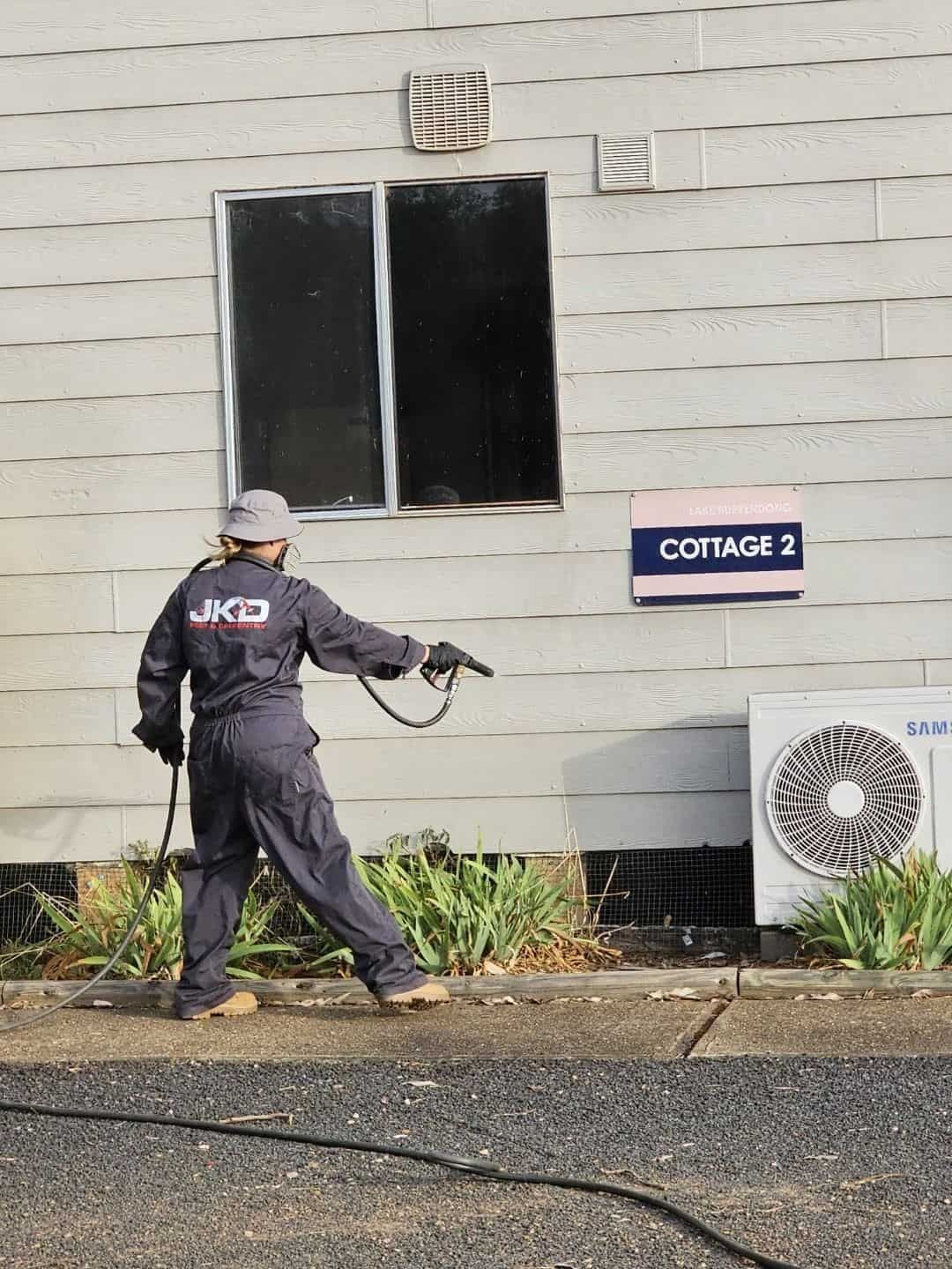 A Man is Cleaning the Side of a Building With a Pressure Washer — JKD Pest & Carpentry In Wellington, NSW