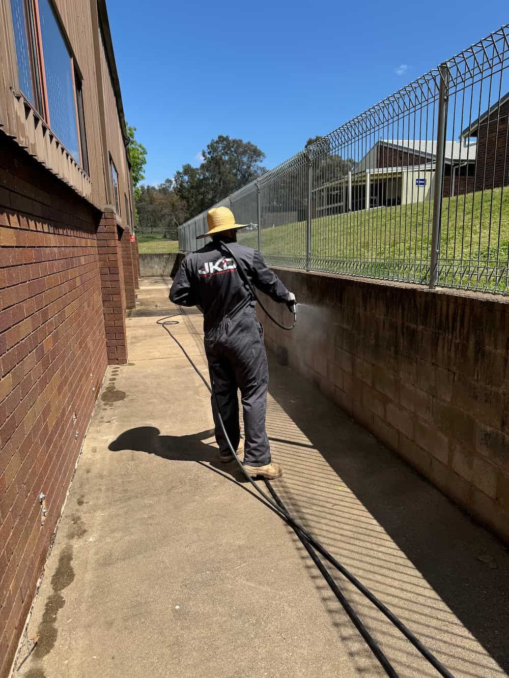 A Man is Spraying a Brick Wall With a Hose — JKD Pest & Carpentry In Parkes, NSW