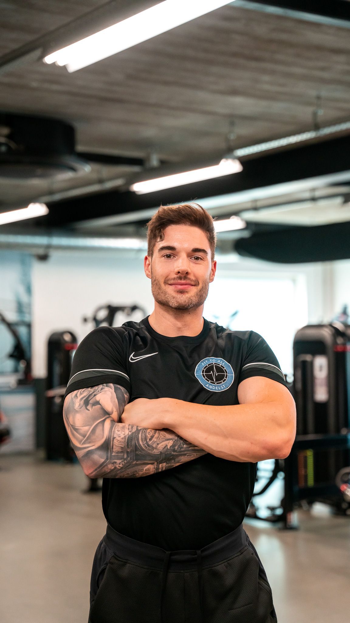 Een man in een zwart Nike-shirt staat met zijn armen over elkaar in een sportschool.
