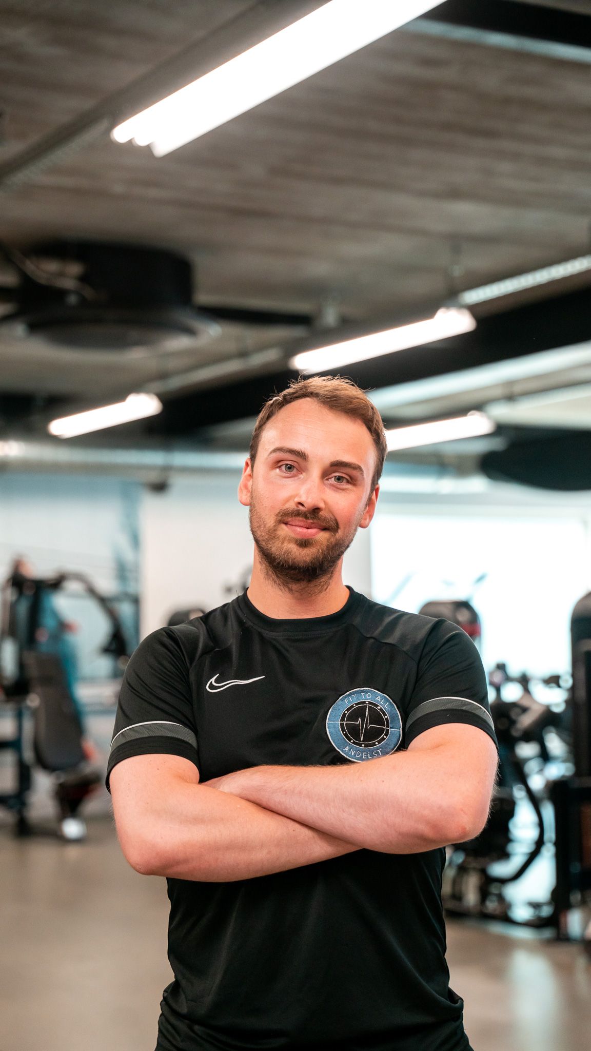 Een man met een baard zit in een stoel in een sportschool en draagt ​​een zwart Nike-shirt.