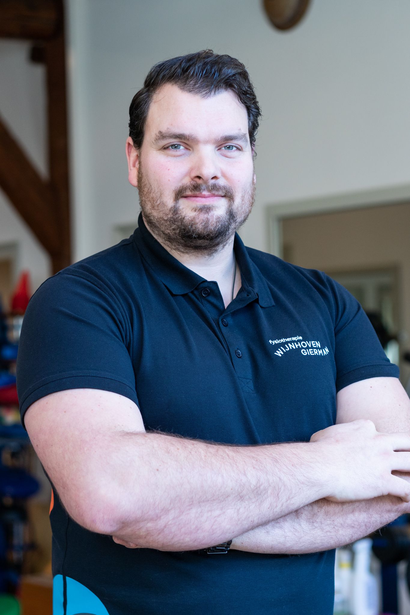 Een man met een baard staat met zijn armen over elkaar in een kamer.