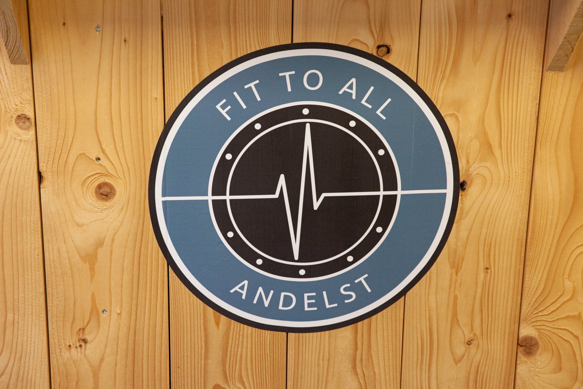Het logo voor fit to all andelst staat op een houten muur