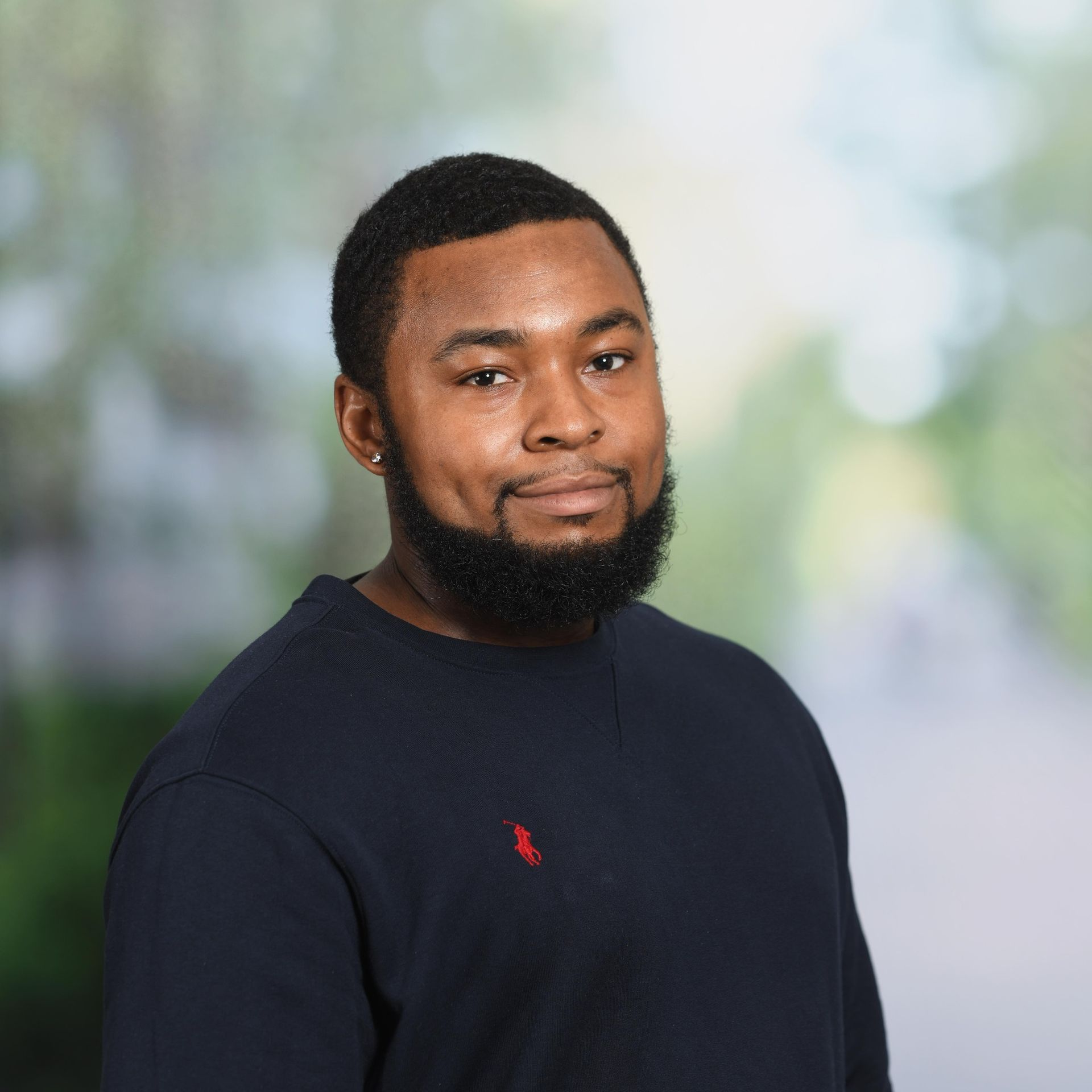 Man with a dark beard and short haircut wearing a dark blue sweater, smiling.