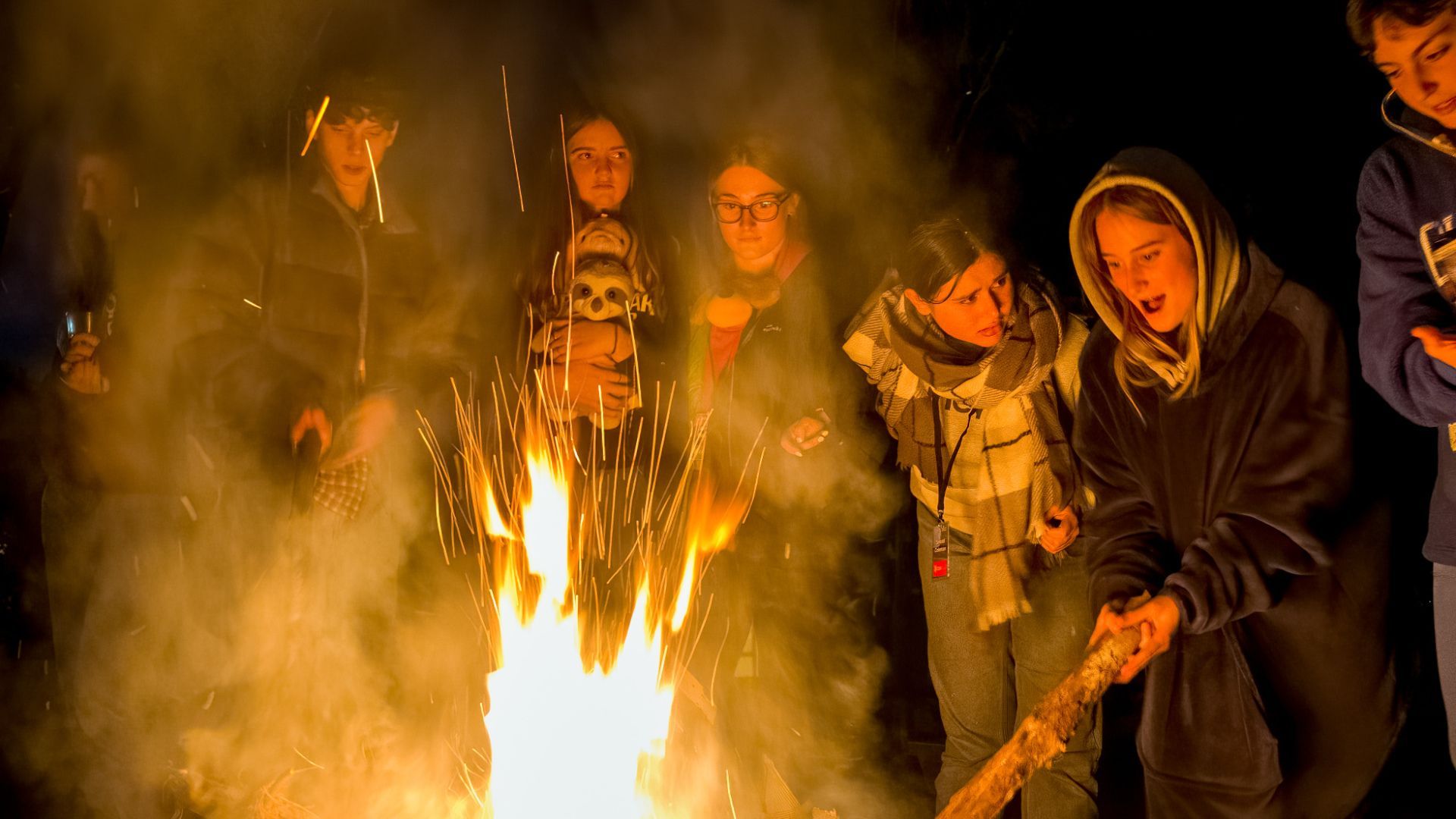 A group of people are standing around a campfire at night.