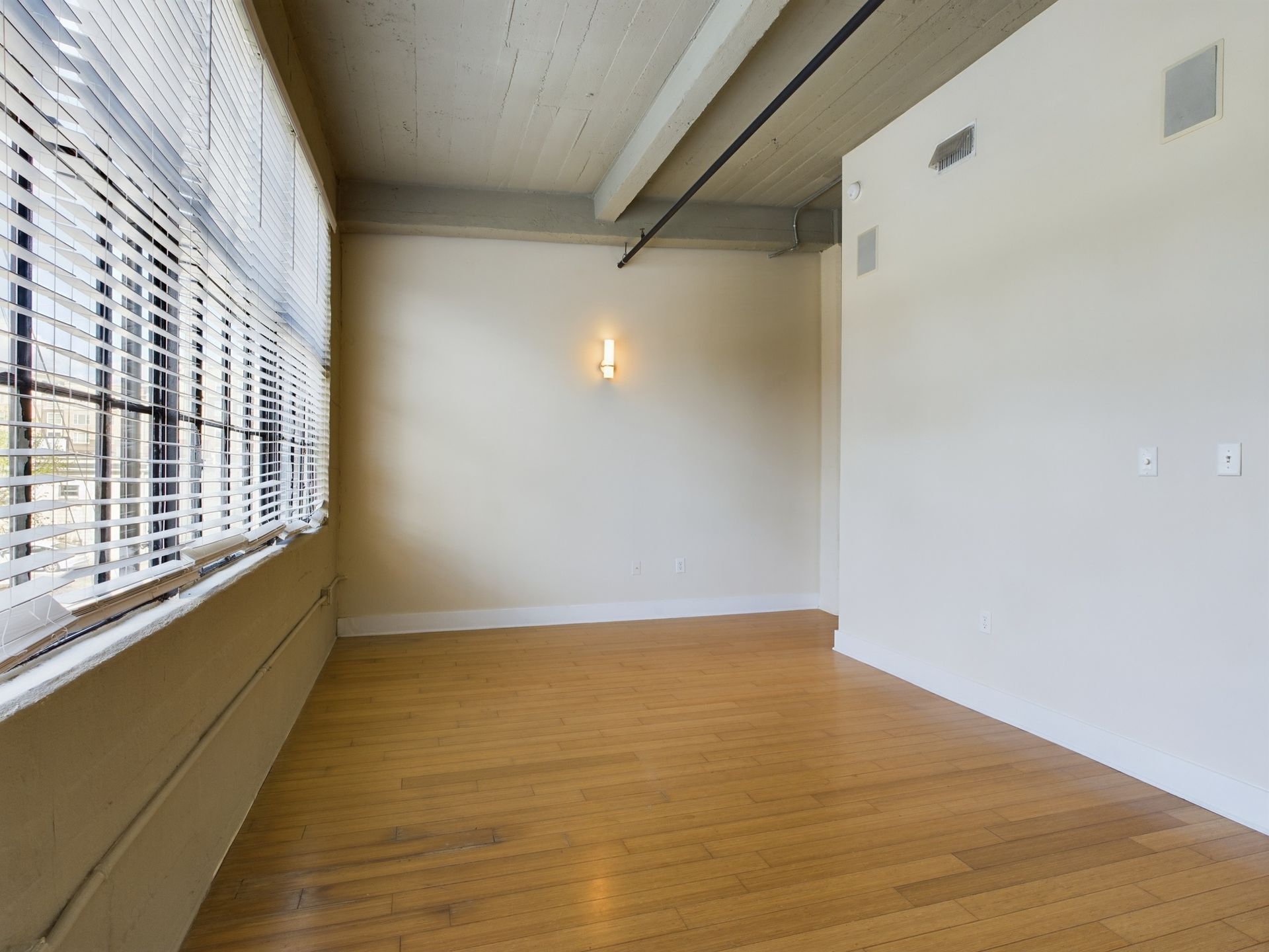 An empty room with wooden floors and blinds on the windows