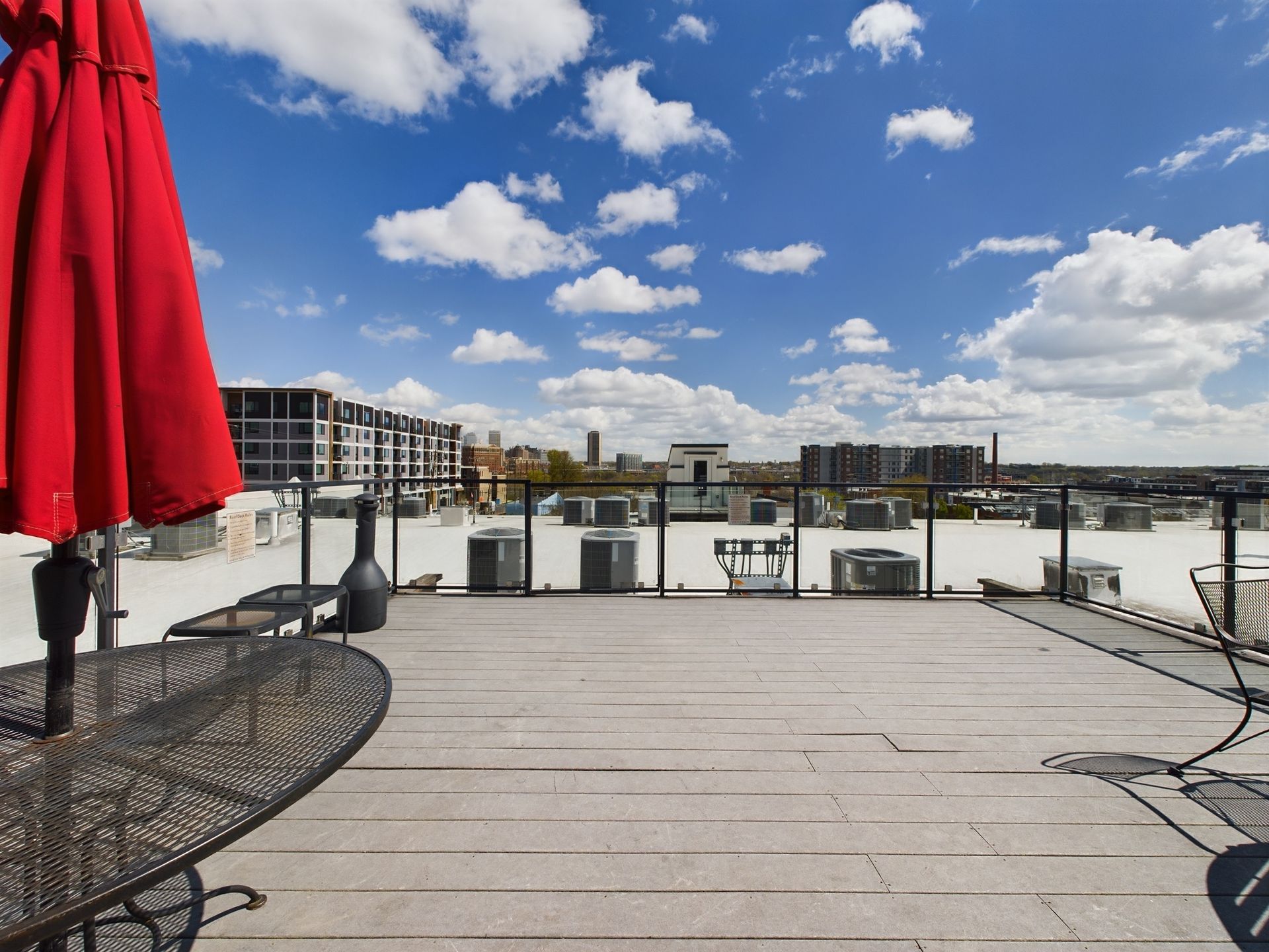A rooftop deck with a table and chairs and a red umbrella
