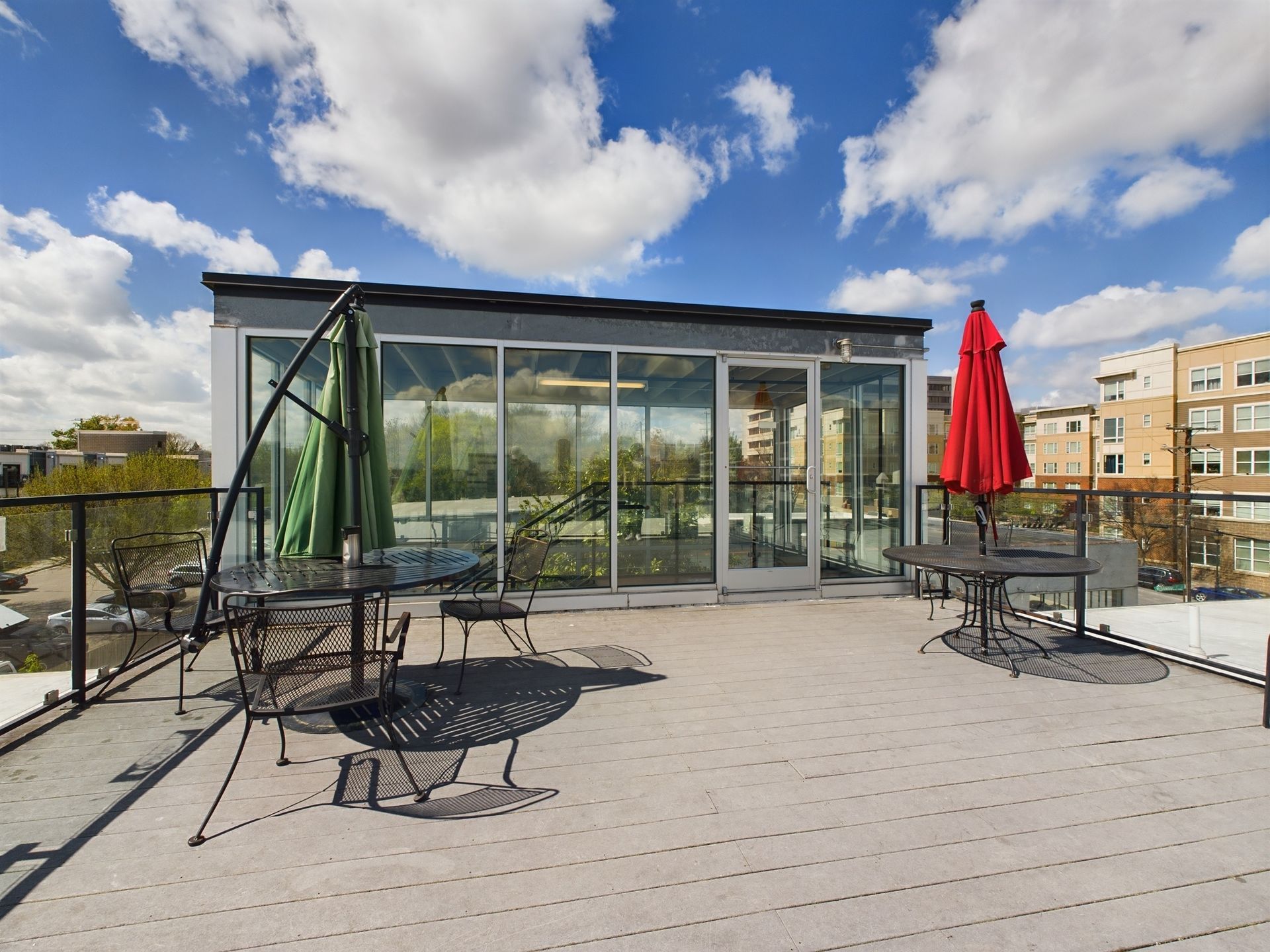 A rooftop deck with tables and chairs and a red umbrella