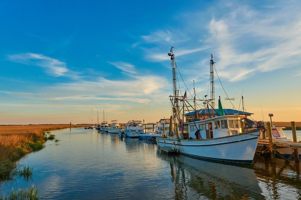 A row of boats are docked in a harbor at sunset.