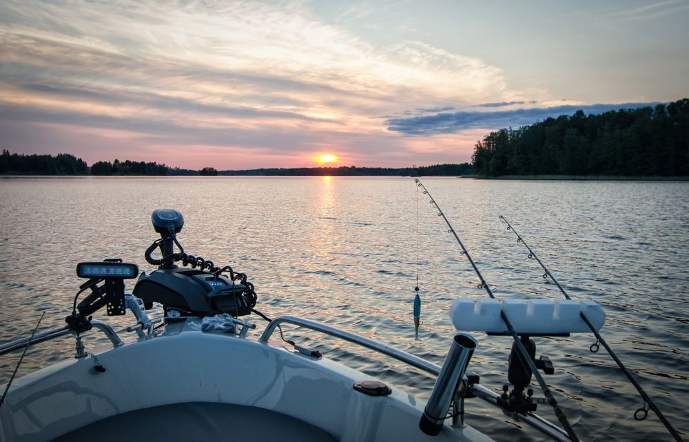A boat with a motor and fishing rods is floating on a lake at sunset.