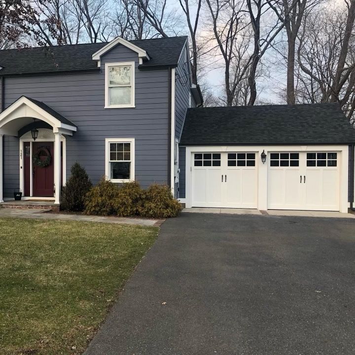 A blue house with white garage doors and a black roof