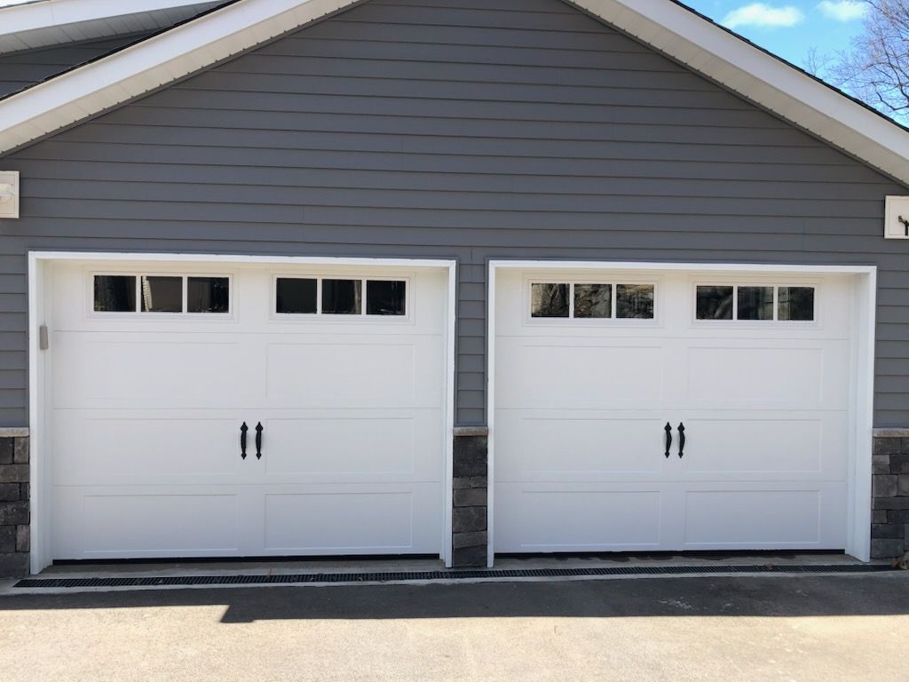 Two white garage doors are sitting next to each other on the side of a house.