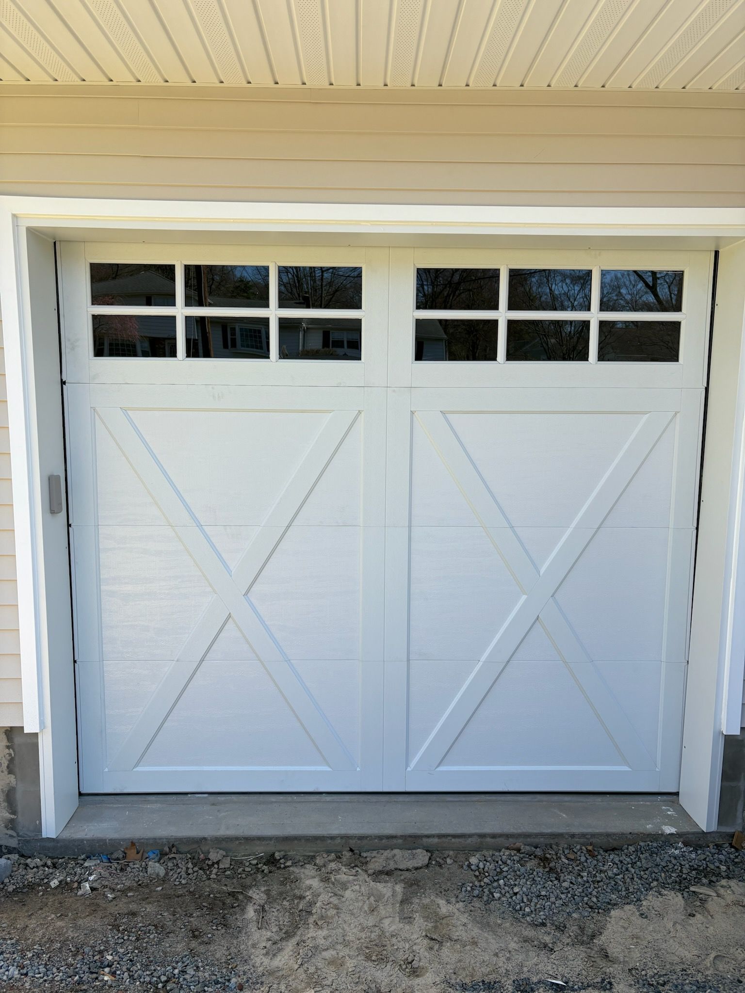 A white garage door with a cross on it is sitting in front of a house.