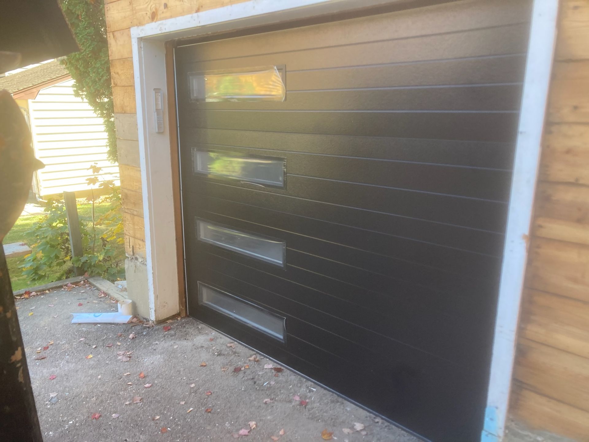 A black garage door is sitting in front of a wooden building.