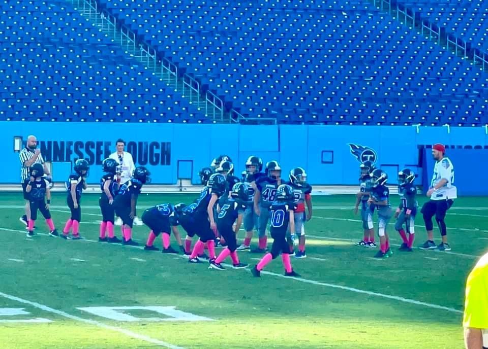 A group of young boys are playing football in front of a blue wall that says tennessee rough