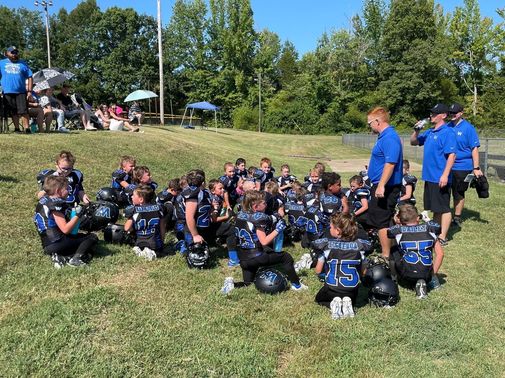 A group of young football players are sitting on the grass on a field.