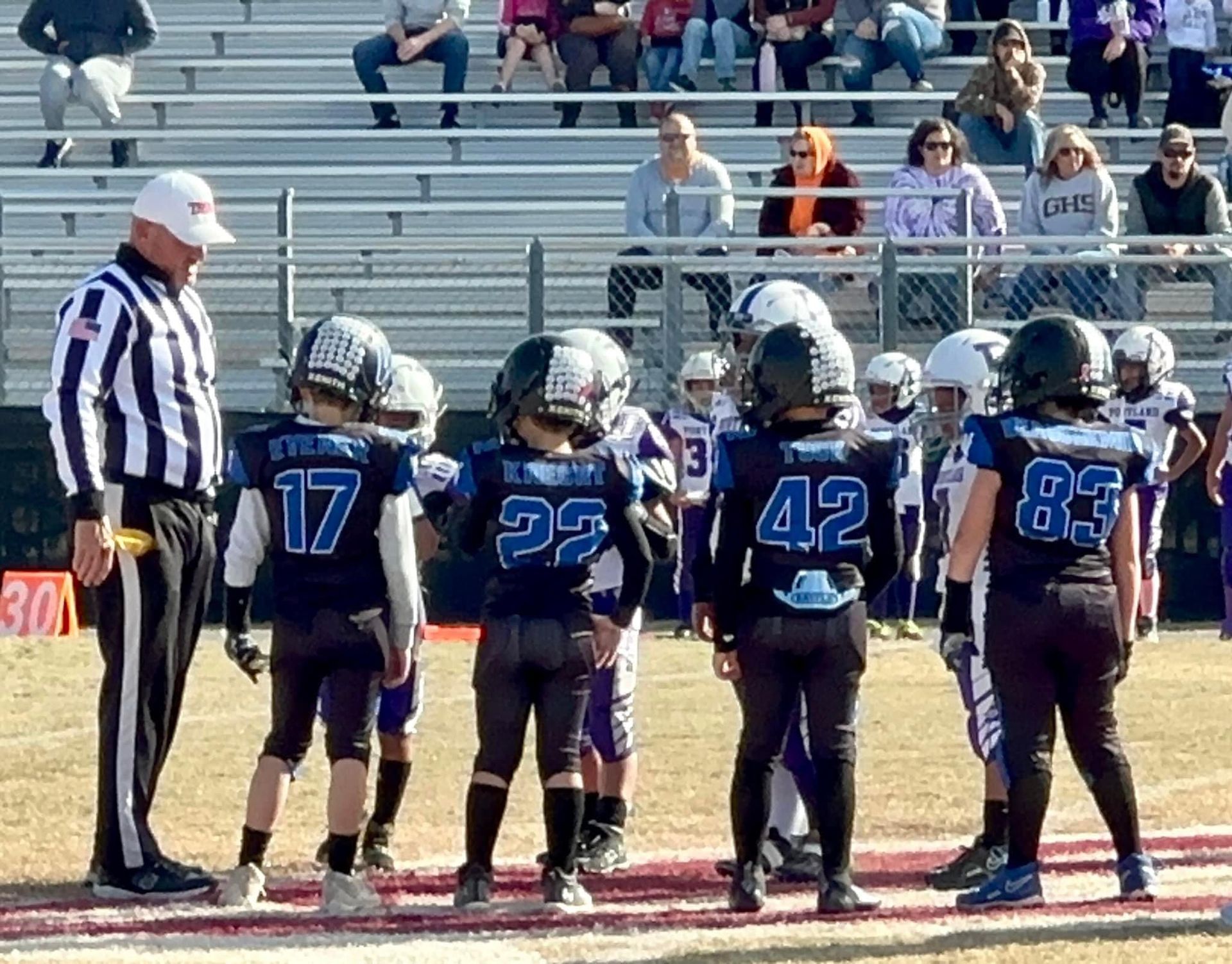A group of young football players standing in a huddle with a referee